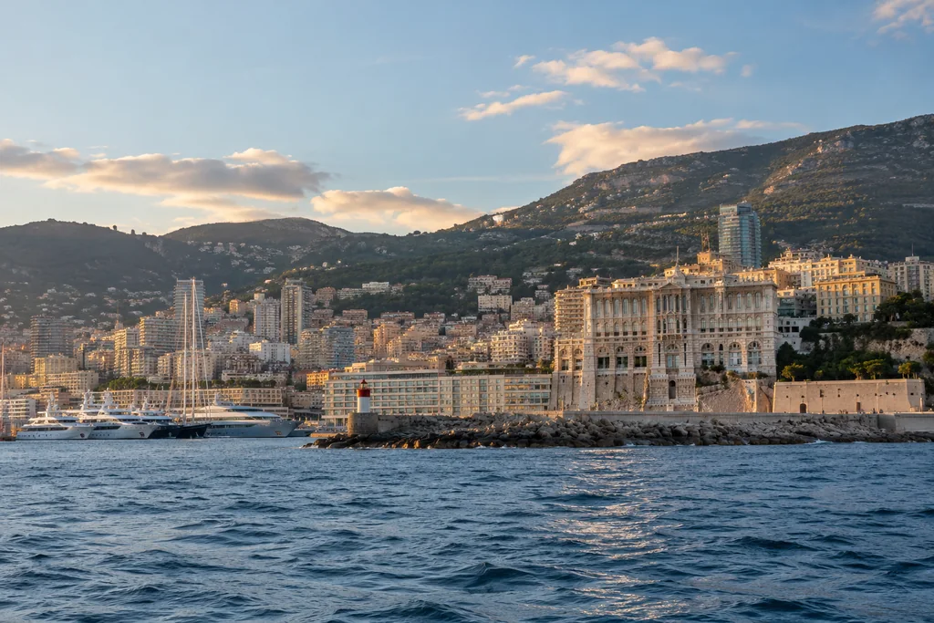 The Monaco waterfront from offshore at late afternoon, elegant coastal buildings and harbour breakwater, accurate Mediterranean atmosphere